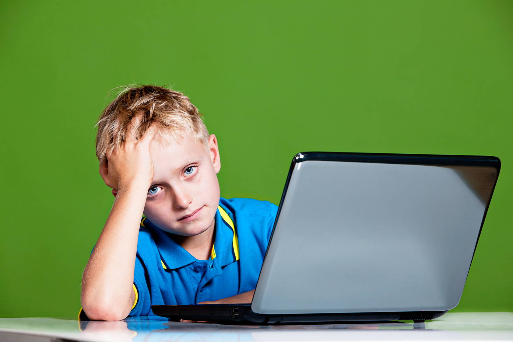 Blond schoolboy looks up from laptop looking worried