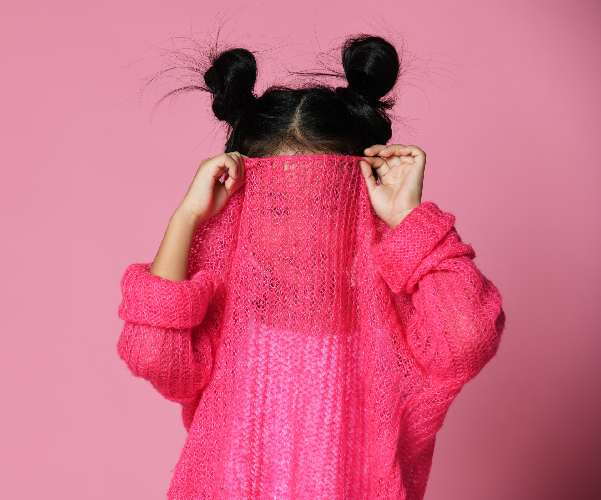 Kid girl hides her face in pink sweater